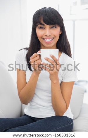 Calm beautiful woman holding a cup smiling at camera sitting in bright living room