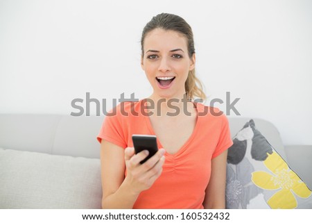 Happy casual woman holding her smartphone sitting on couch in the living room