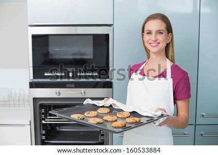 Casual happy woman holding baking tray with cookies in bright kitchen