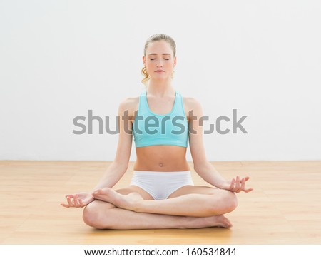Peaceful slim blonde sitting in lotus pose in bright room