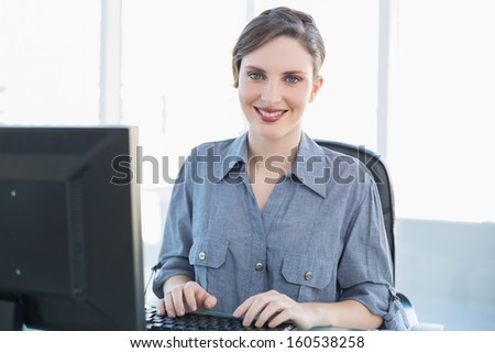 Content businesswoman working on computer at her desk smiling at camera