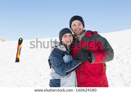 Portrait of a happy loving couple with ski board on snow in background against clear blue sky