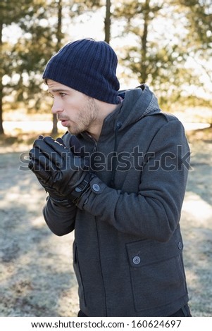 Young man in warm clothing shivering while having a walk in forest on a winter day