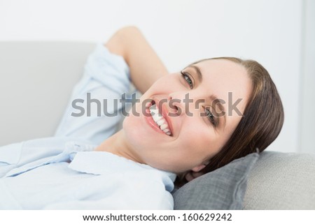 Close-up portrait of a smiling well dressed young woman relaxing on sofa at home