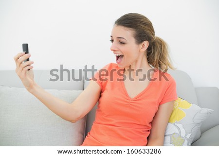 Surprised casual woman looking at her smartphone sitting on couch