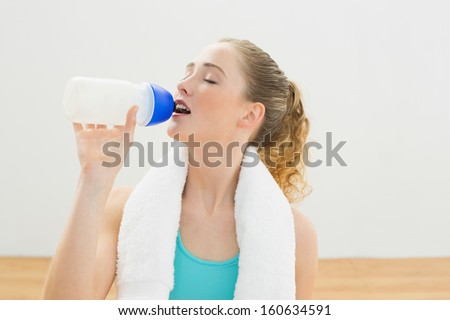 Content slim blonde sitting on floor drinking from sports bottle in bright room