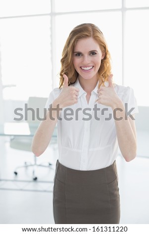 Portrait of a smiling young businesswoman gesturing thumbs up at bright office
