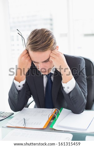 Worried young businessman looking down at documents in office