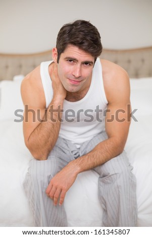Portrait of a young man suffering from neck ache in bed at home
