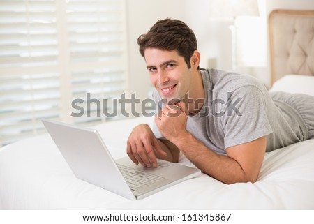 Portrait of a casual smiling young man using laptop in bed at home