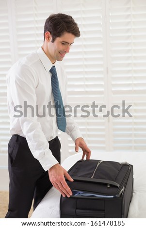 Side view of a smiling businessman unpacking luggage at a hotel bedroom