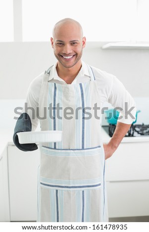 Portrait of a smiling handsome young man holding a baking dish in kitchen
