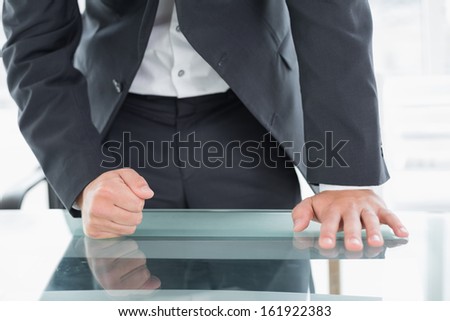 Close up mid section of a well dressed businessman with clenched fist on the desk at office