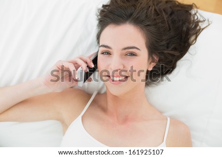 High angle portrait of a relaxed young woman using mobile phone in bed at home