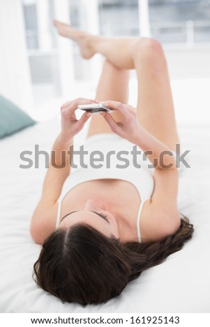 Relaxed young woman looking at mobile phone in bed at home