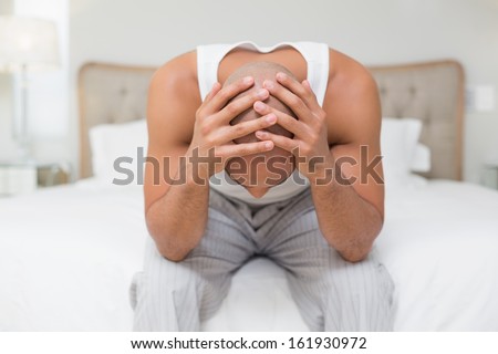 Thoughtful young bald man sitting with head in hands on bed at home
