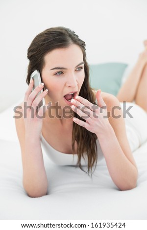 Sleepy young woman yawning while using mobile phone in bed at home