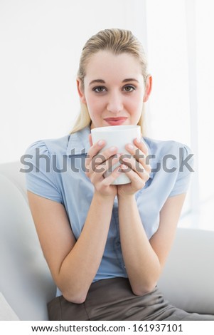 Gorgeous calm businesswoman holding a cup smelling a cup smiling at camera