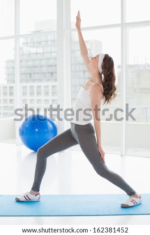 Full length a fit young woman stretching hand in a bright fitness studio