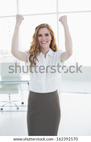 Portrait of a cheerful elegant businesswoman cheering with hands raised in a bright office