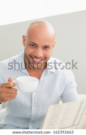 Portrait of a smiling young man having coffee while reading newspaper at home