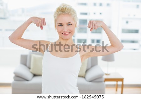 Portrait of a fit young woman in sportswear flexing muscles in a bright fitness studio