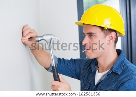 Close up of a serious young handyman hammering nail in wall