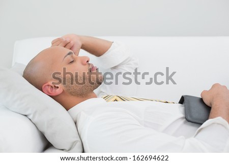 Elegant young businessman sleeping on sofa with digital tablet at home