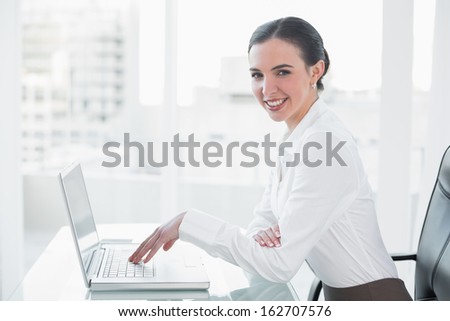 Side view portrait of a smiling businesswoman using laptop at desk in a bright office