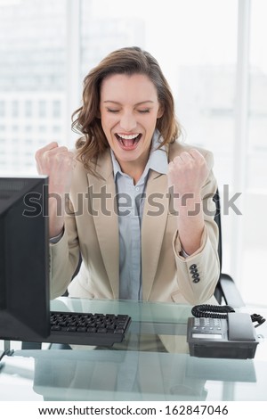 Elegant businesswoman cheering with clenched fists and eyes closed in office