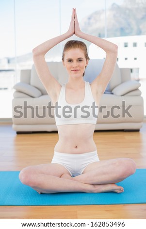 Portrait of a smiling young woman with joined hands over head at fitness studio