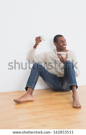 Full length of a casual Afro young man having tea on floor in an empty room