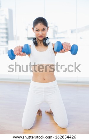 Portrait of a fit young woman exercising with dumbbells in bright fitness studio
