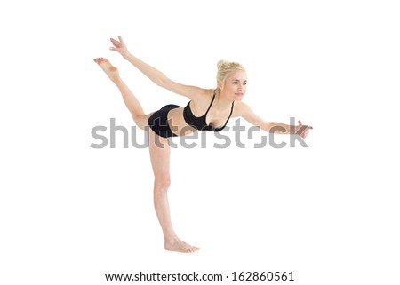 Full length side view of a sporty young woman balancing on one leg over white background