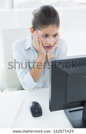 Worried young businesswoman looking at computer in a bright office
