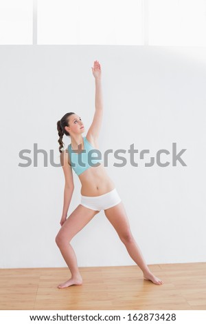 Full length of a sporty young woman stretching hand in fitness studio
