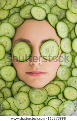 Close up of a young beautiful woman with facial mask of cucumber slices on her face at spa salon