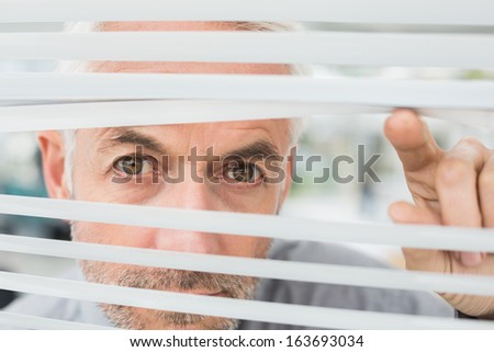 Close-up portrait of a serious mature businessman peeking through blinds in the office