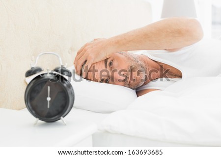 Mature man resting in bed with alarm clock in foreground at bedroom