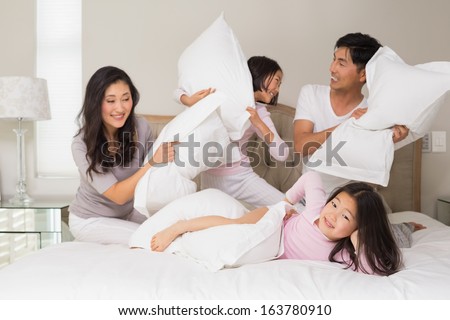Cheerful kids and parents  having pillow fight on bed at home
