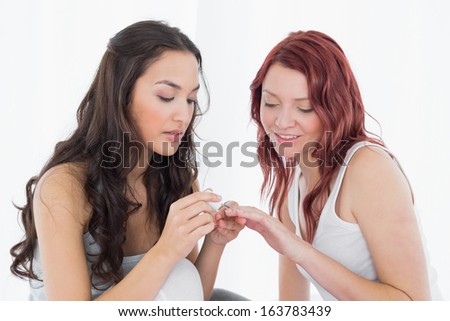 Pretty young woman painting a smiling friend\'s nails in bright bedroom