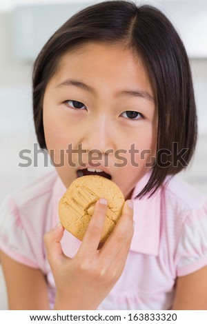 Close-up portrait of a young girl eating cookie in a bright home