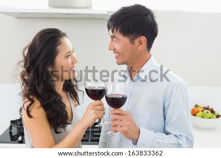 Side view of a loving young couple with wine glasses in the kitchen at home