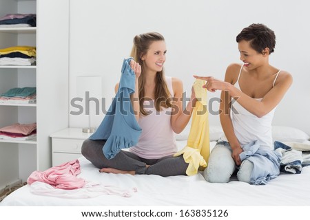 Two pretty female friends selecting clothes in bed at home