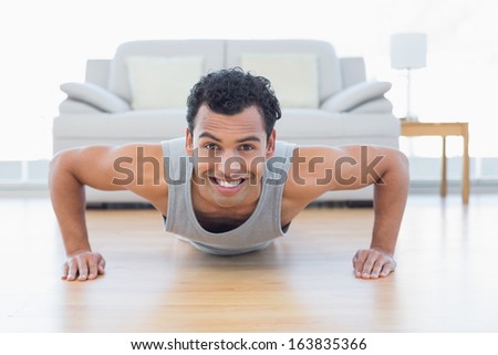 Portrait of a sporty smiling young man doing push ups in the living room at house