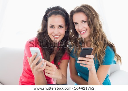 Two smiling young female friends in sunglasses reading text message in the living room at home