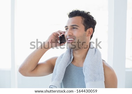Fit young smiling man using mobile phone against bright background
