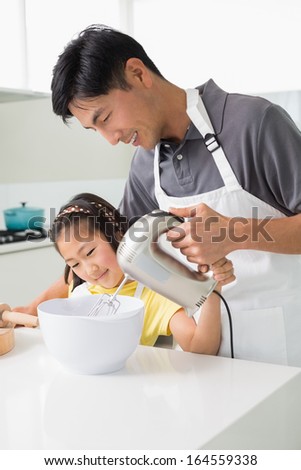 Young man with his daughter using electric whisk into bowl in the kitchen at home