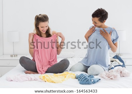 Two pretty female friends selecting clothes in bed at home
