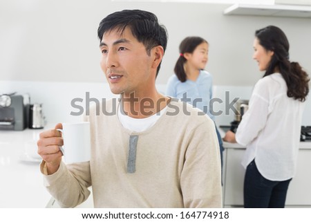 Thoughtful young man drinking coffee with family in background at home